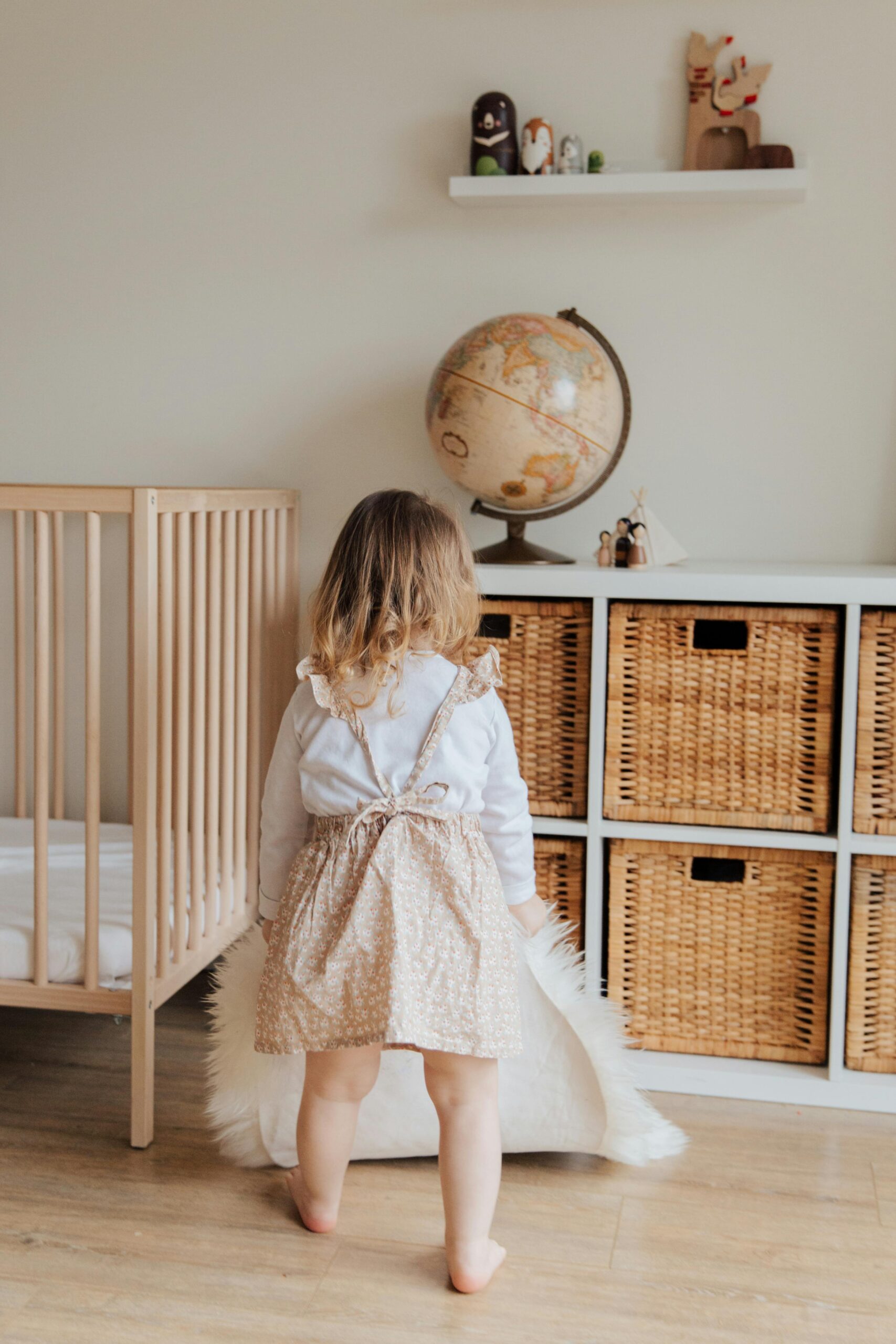 Back view of unrecognizable cute little girl in casual dress holding white carpet in hands while playing in light room at home
